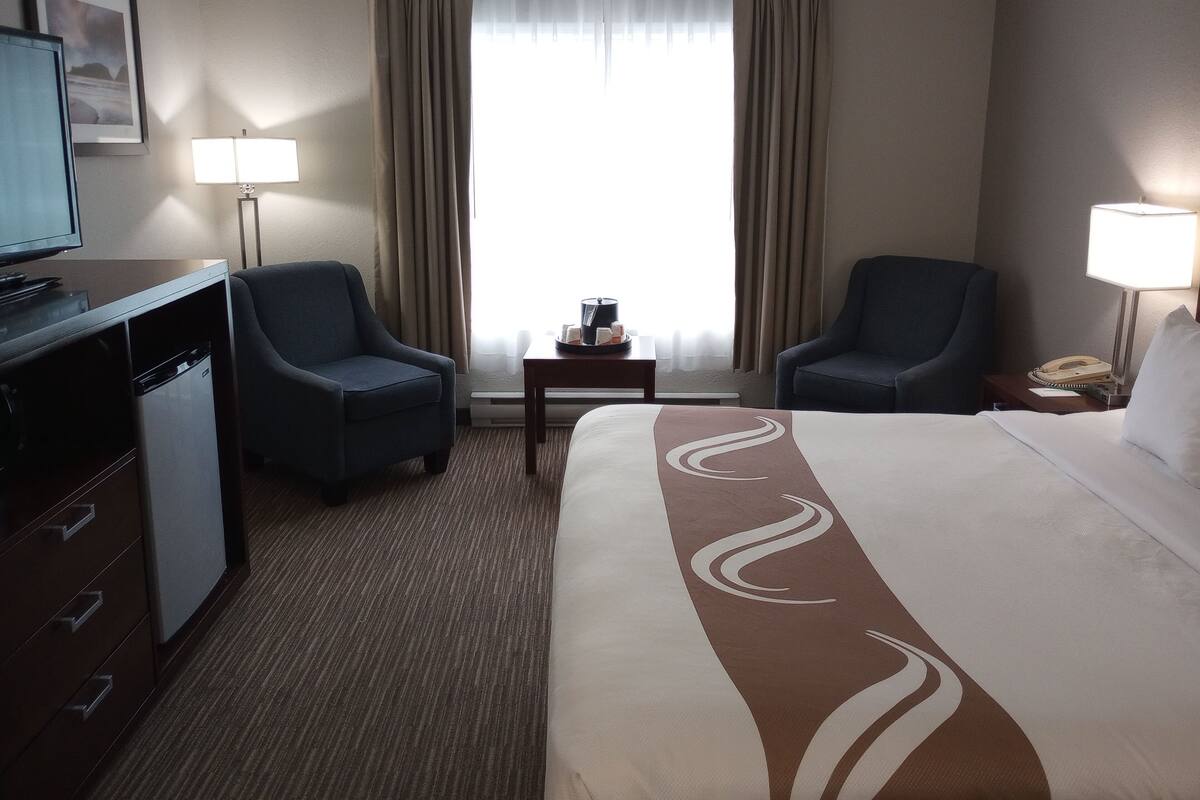 Een hotelkamer met een bed, twee fauteuils, een bureau met een televisie, een lamp en een kleine tafel met een dienblad.