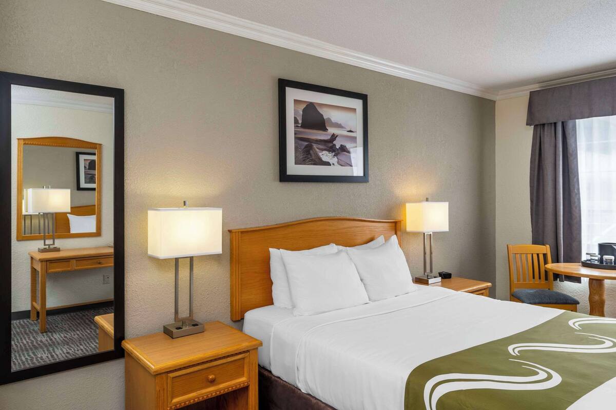 Een hotelkamer met een groot bed, twee nachtkastjes met lampen, een houten bureau, een stoel, een bijzettafeltje en een lijst aan de muur.