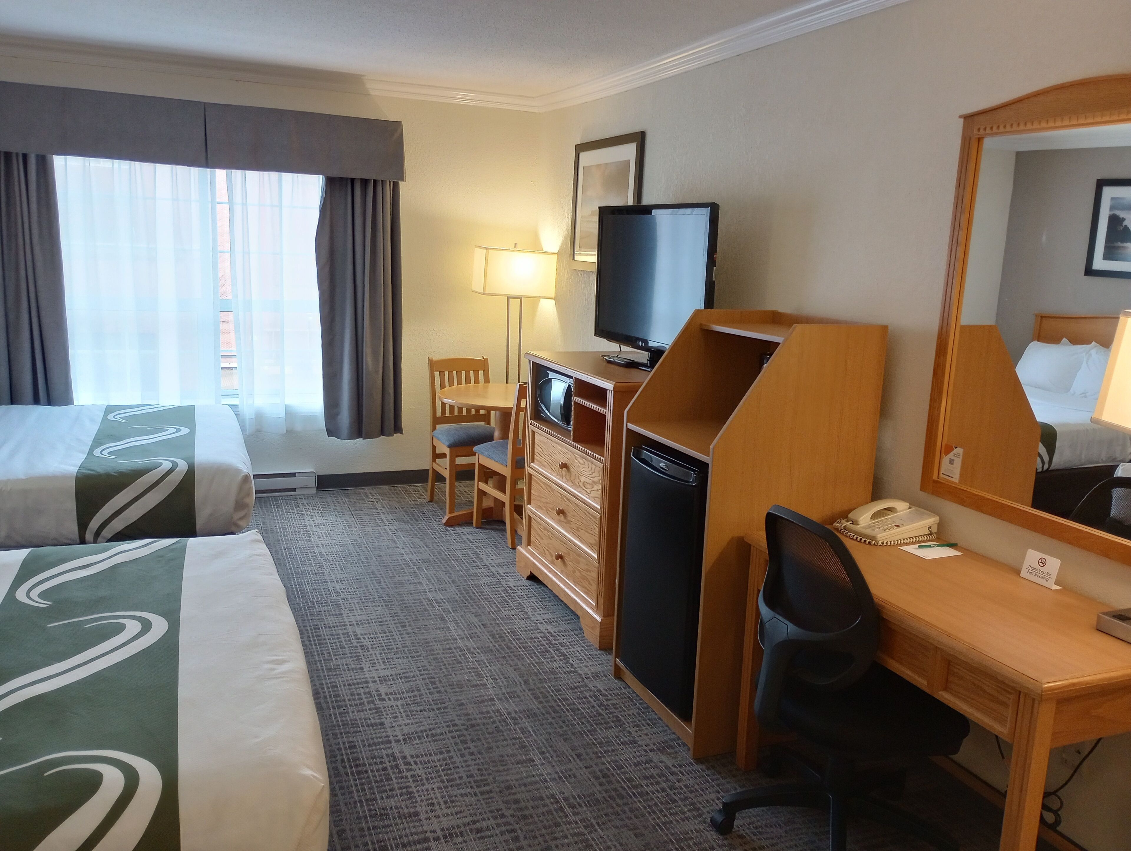 Een hotelkamer met een bed, een bureau, een stoel, een televisie, een lamp en een spiegel.