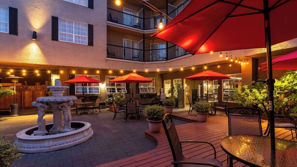 An outdoor patio area with red umbrellas, seating, and a central fountain.