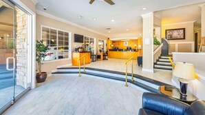A spacious lobby with a marble floor, a reception desk, a staircase, and a seating area.