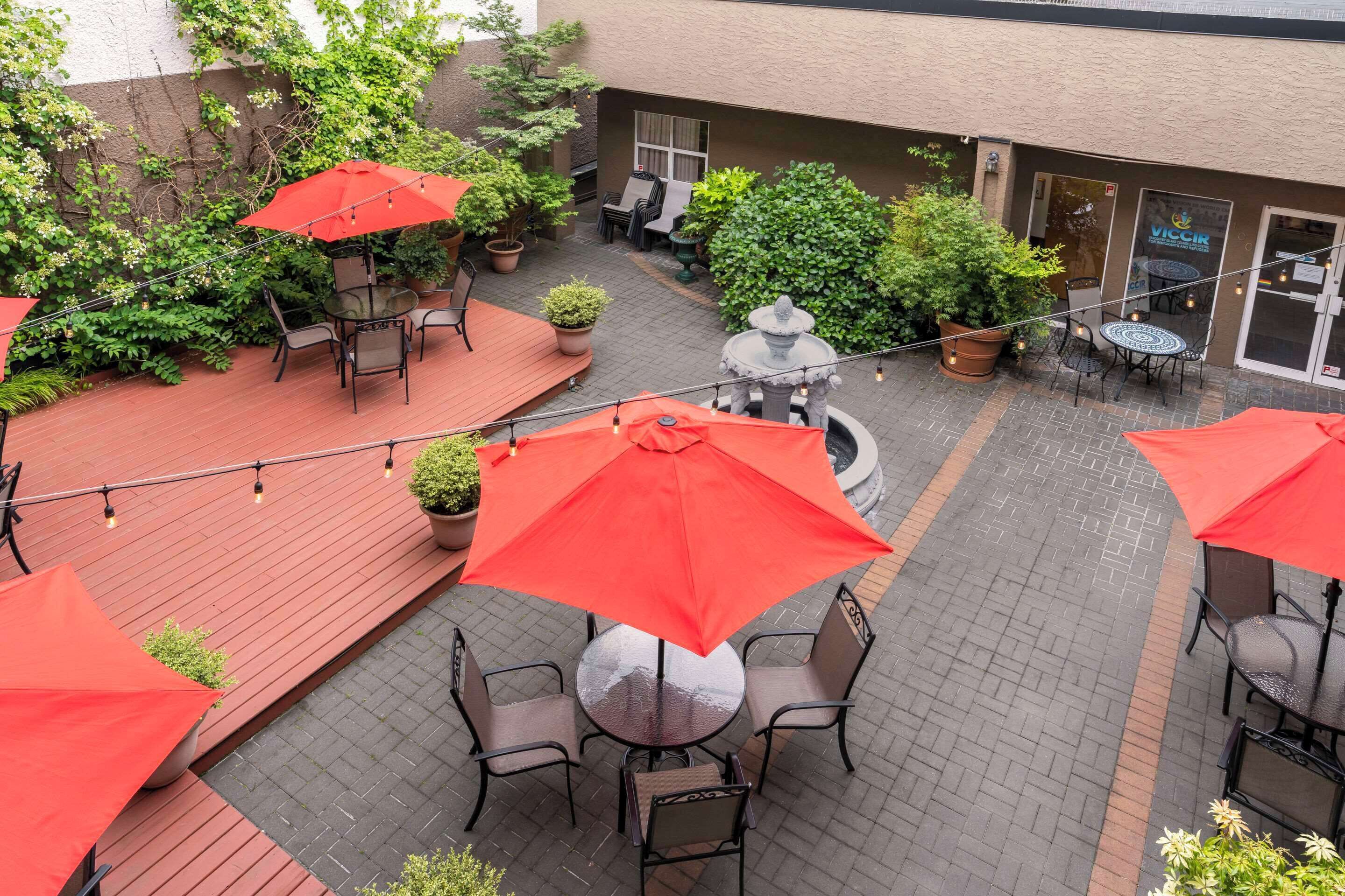 An outdoor patio area with tables and chairs, red umbrellas, and potted plants.