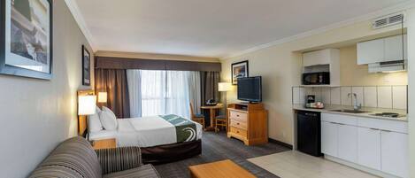 Habitación de hotel con cama, sofá, televisión, escritorio y kitchenette.