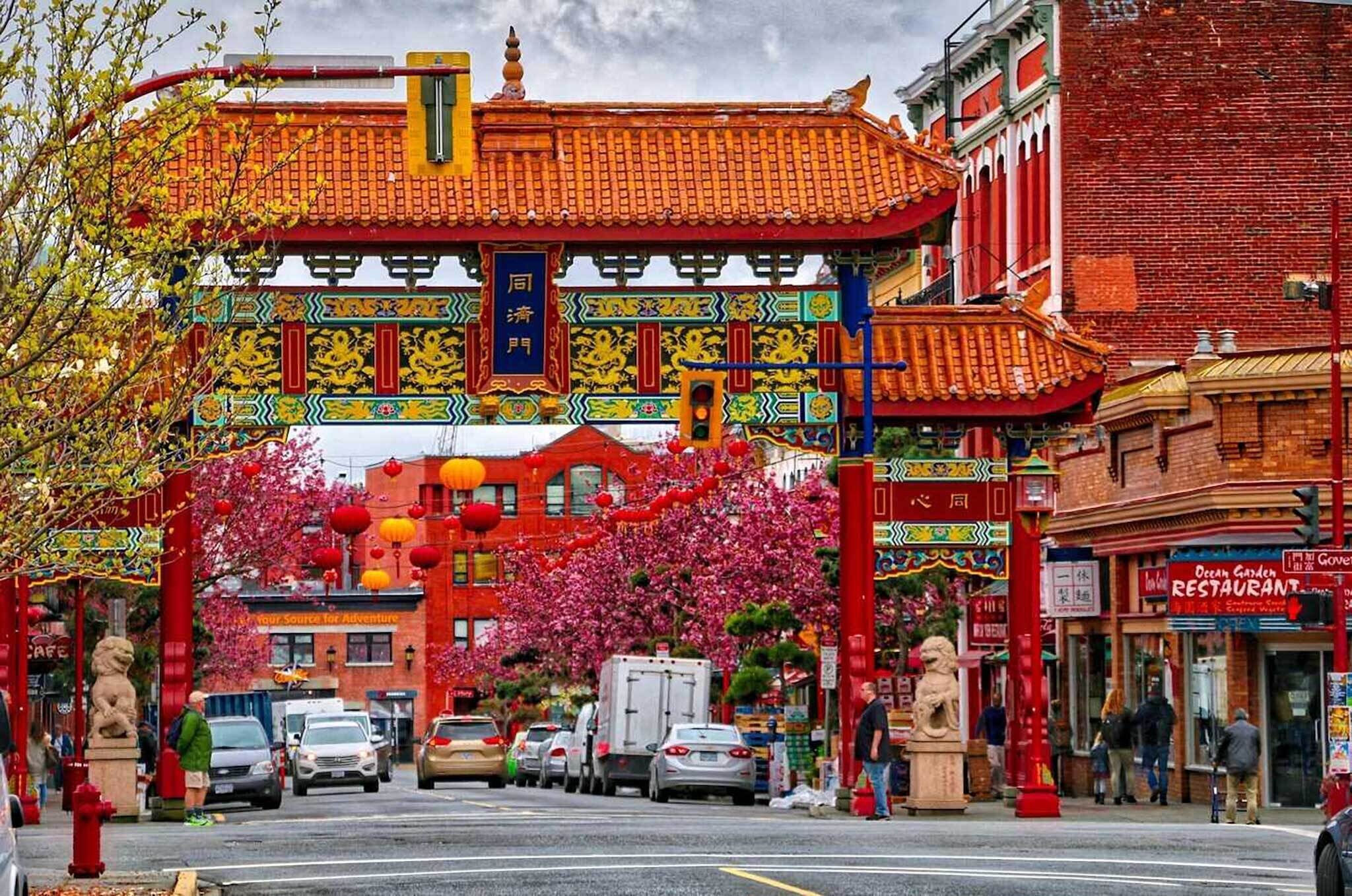 Una calle con una puerta tradicional china, automóviles estacionados y un restaurante llamado 'Ocean Garden Restaurant'.