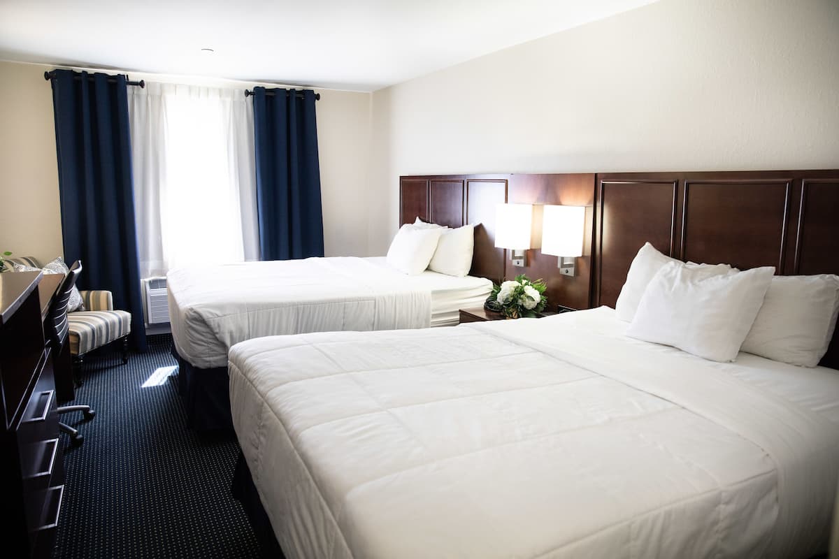 A hotel room with two beds, a desk, and a chair.