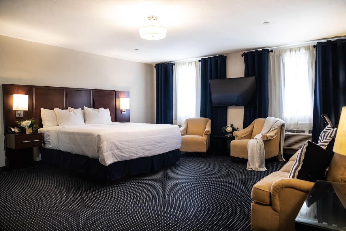 A hotel room with a large bed, two armchairs, a TV, and a flat-screen TV mounted on the wall.