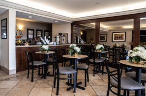 A restaurant with round tables and chairs, a coffee station, and framed pictures on the walls.