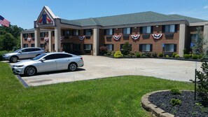 A hotel with a brick facade, American flags, and a parking lot with two cars.