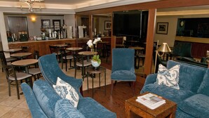 Um saguão de hotel com um conjunto de sofás azuis, um bar de café e uma televisão.