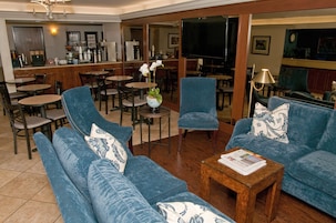 Un vestíbulo de hotel con un conjunto de sofá azul, una barra de café y un televisor.