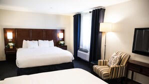 Quarto de hotel com uma cama grande, uma cadeira, uma escrivaninha, uma televisão e um abajur.