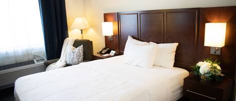 Habitación de hotel con una cama grande, dos lámparas de noche, un teléfono y una mesita de noche con un jarrón de flores.