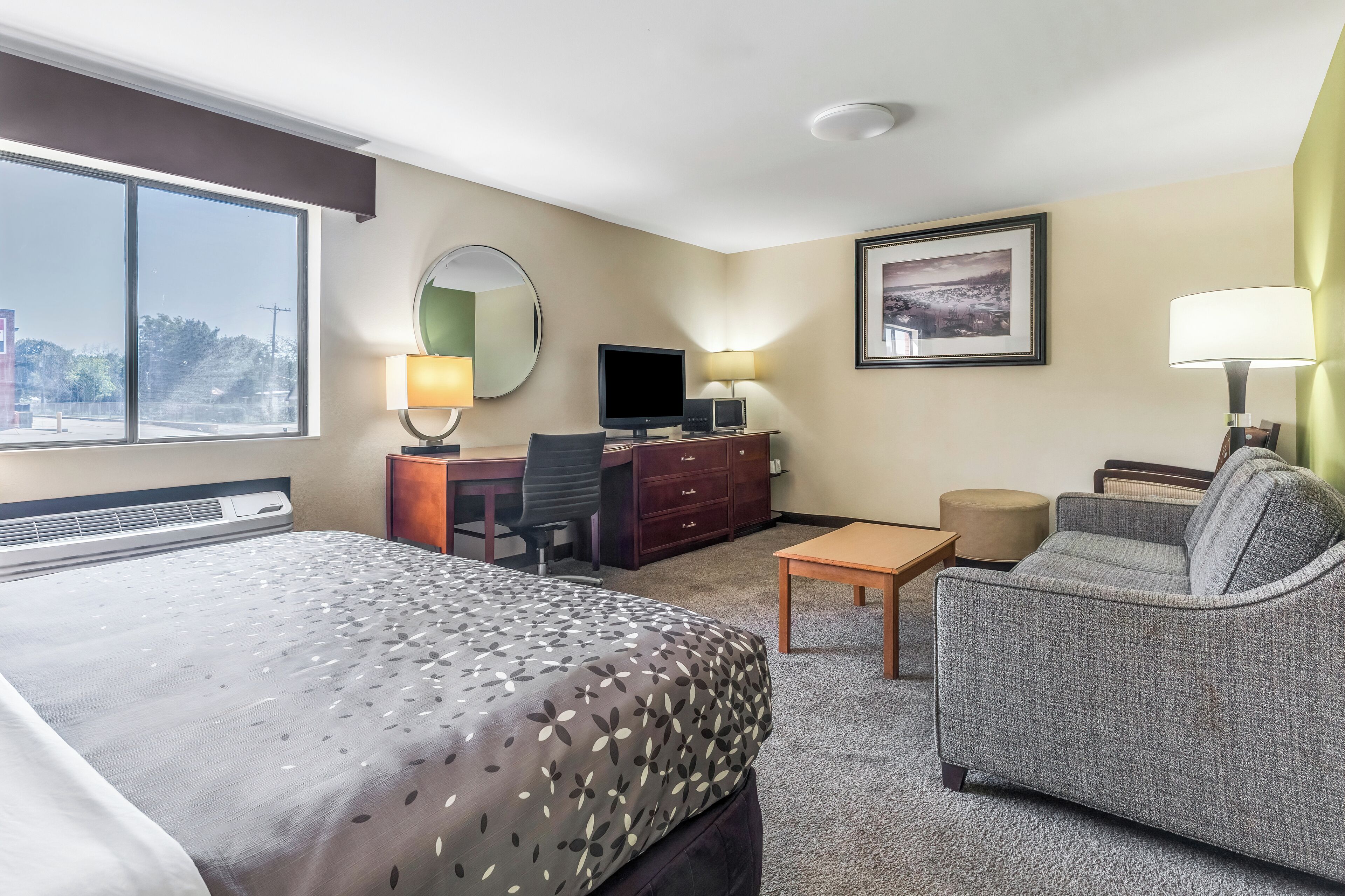 A hotel room with a large bed, a desk with a computer, a sofa, and a TV.