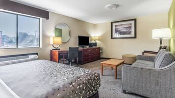 A hotel room with a large bed, a desk with a computer, a sofa, and a TV.