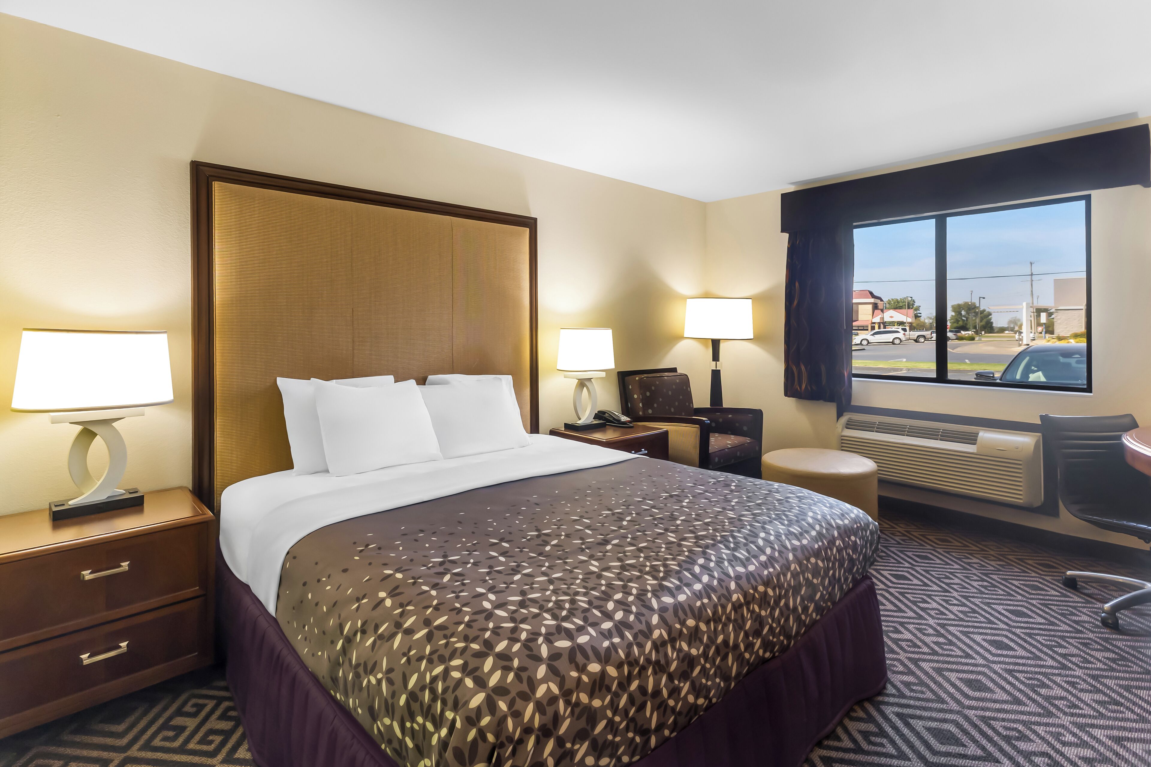 A hotel room with a large bed, two bedside tables with lamps, a chair, and a view of the street through a large window.
