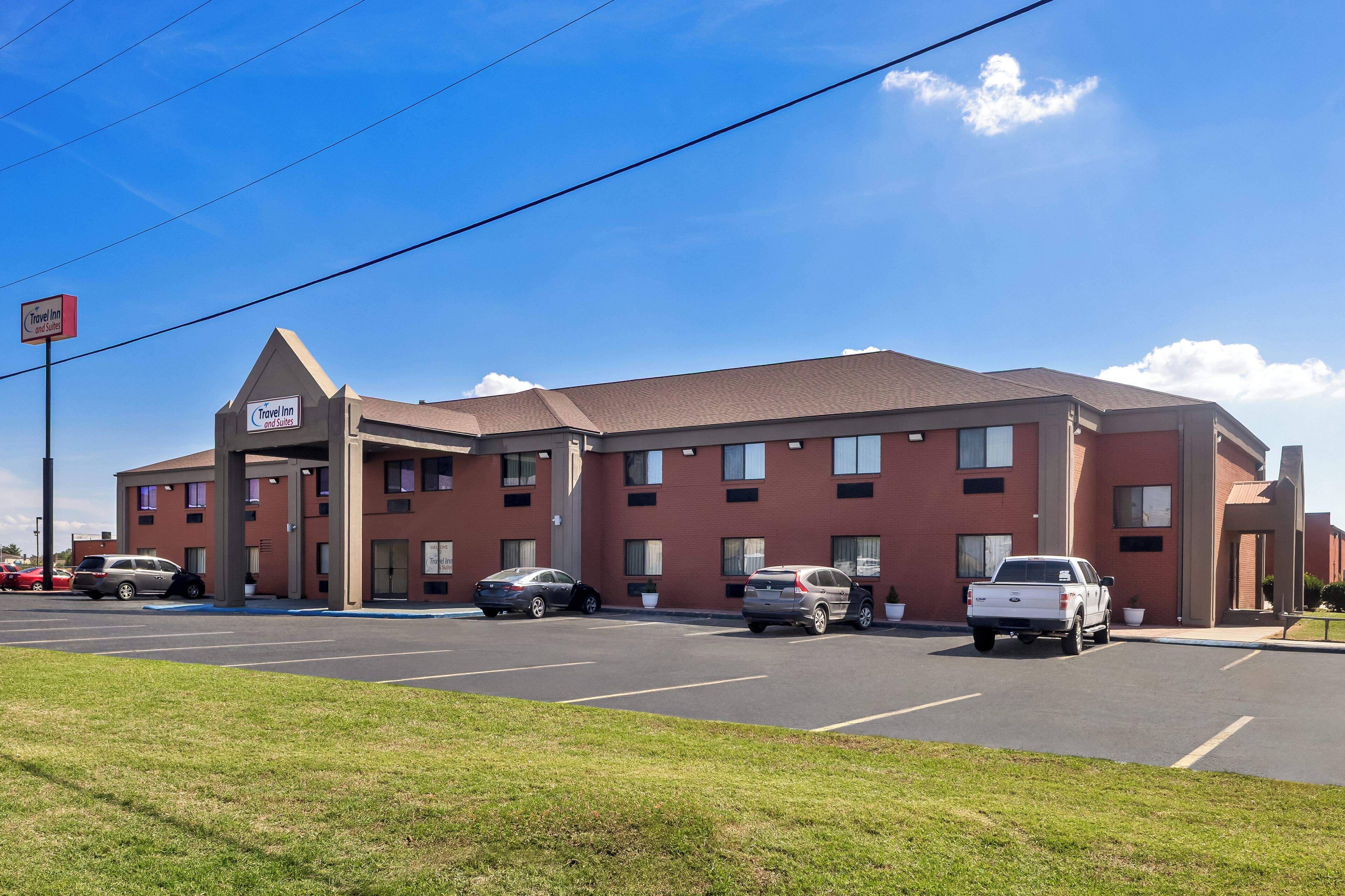 A Travel Inn with a parking lot, multiple cars, and a clear blue sky.