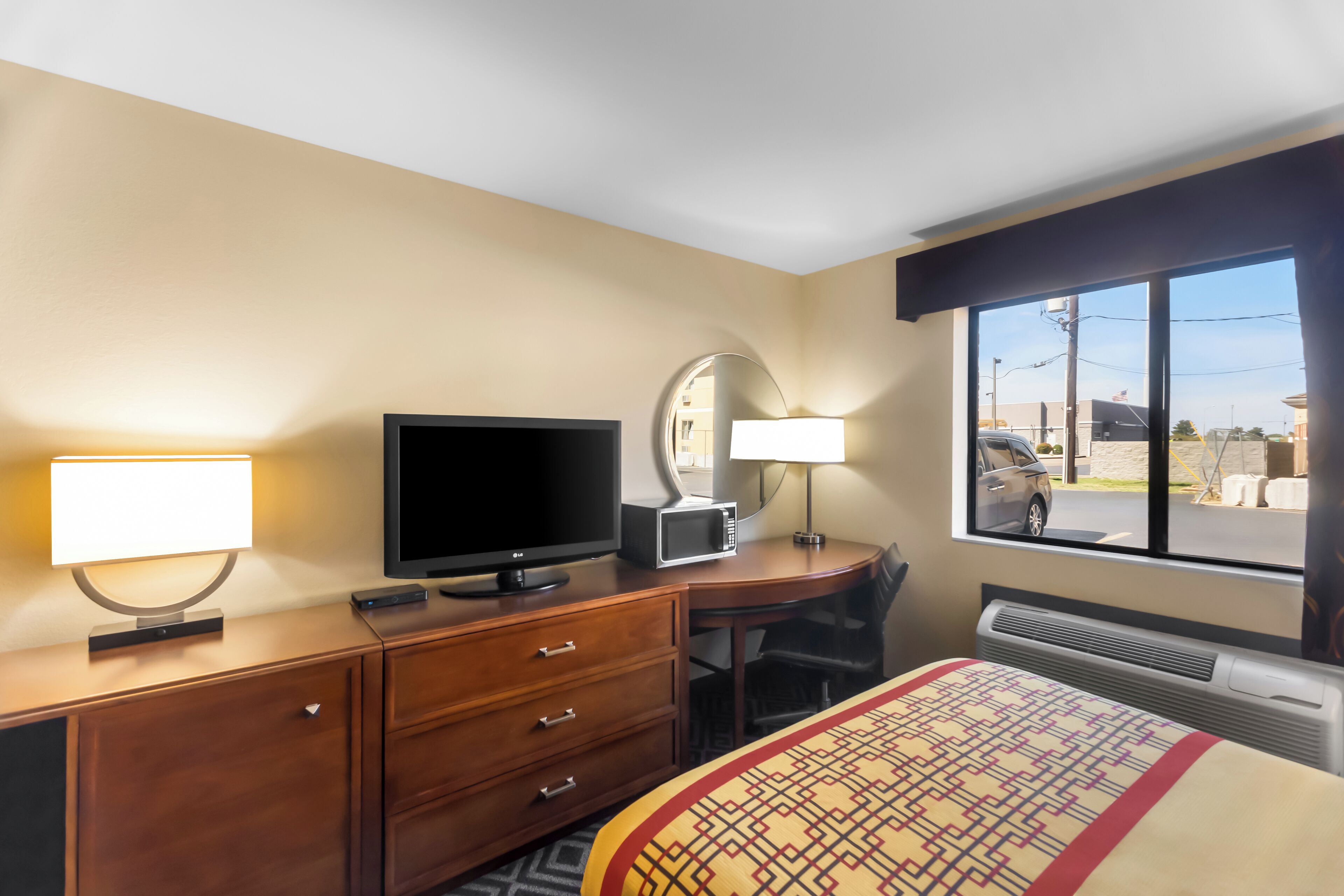 Ein Hotelzimmer mit Bett, Schreibtisch mit Computer, Fernseher, Mikrowelle, Lampe und Fenster mit Blick ins Freie.