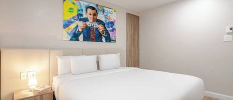 A hotel room with a large bed, a nightstand with a lamp, and a colorful painting on the wall.