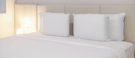 A neatly made bed with white bedding and pillows, a bedside lamp, and a wall with abstract art.