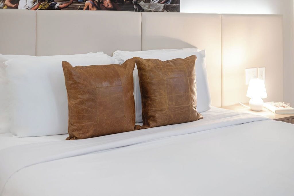 A neatly made bed with white linens and two brown pillows.