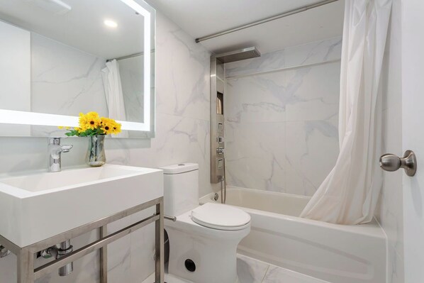 A modern bathroom with a white marble sink, a toilet, and a bathtub. - Olympia Hotel By Lodgo (Montreal)