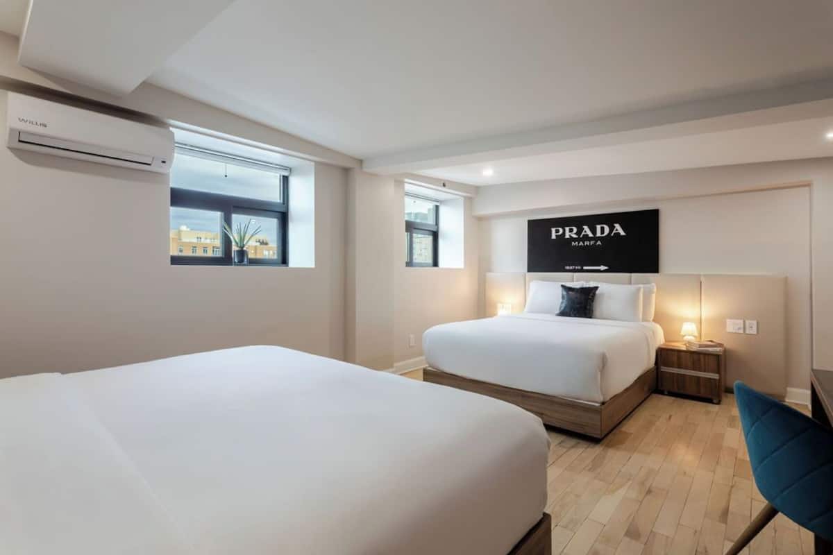 A hotel room with two beds, a Prada sign, and a Willis air conditioning unit.