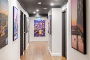 A hallway with framed artwork on the walls, a cityscape painting at the end, and a directional sign. - Olympia Hotel By Lodgo (Montreal)