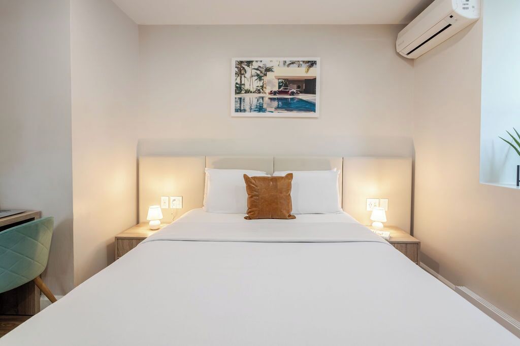 Ein Hotelzimmer mit einem großen Bett, zwei Nachttischen mit Lampen, einer Wand-Klimaanlage und einem gerahmten Bild über dem Bett.