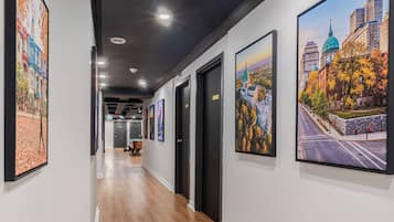 A hallway with wooden flooring, black-framed artwork on the walls, and a ceiling with recessed lighting.