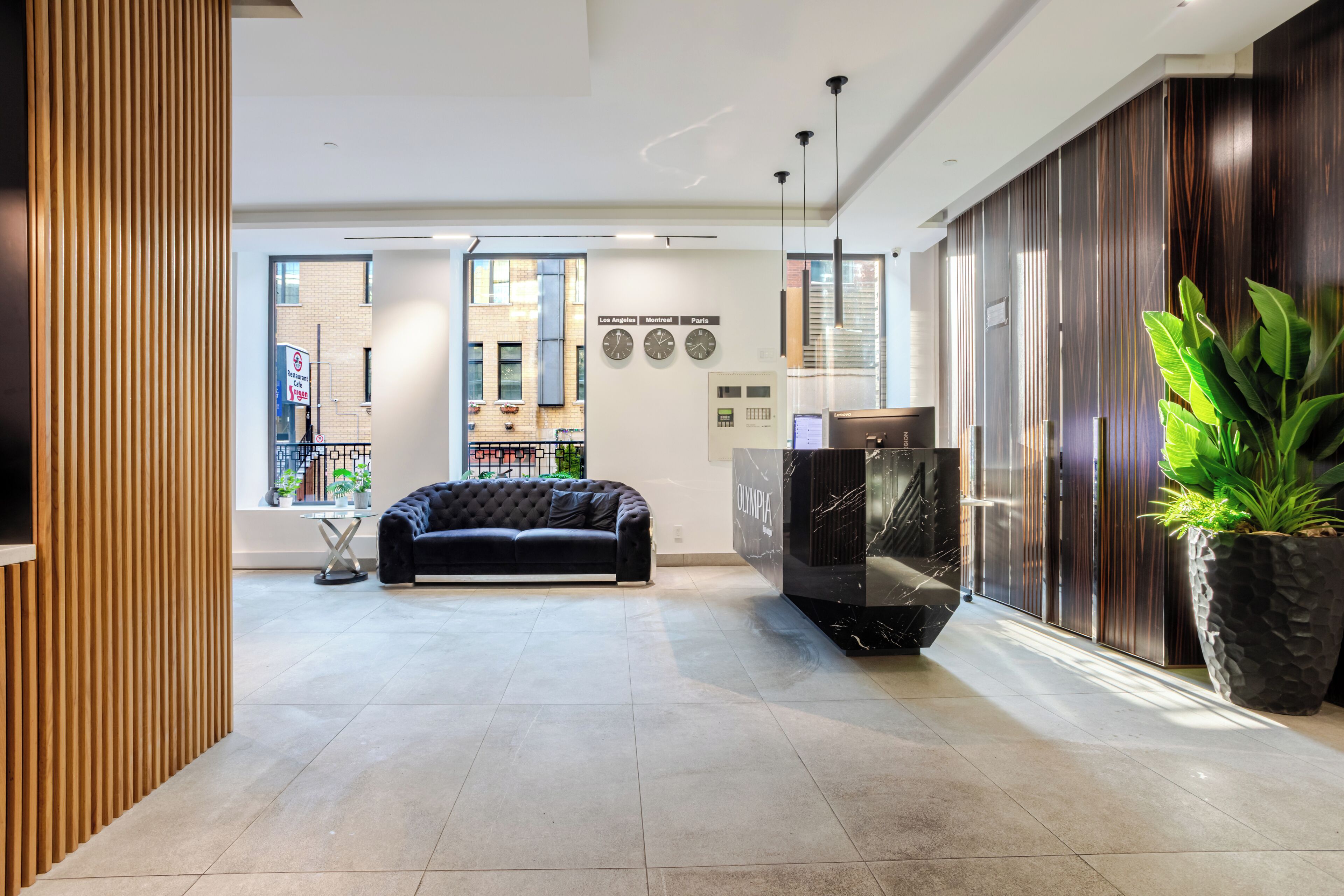 A modern lobby with a black sofa, a reception desk, and a large potted plant.