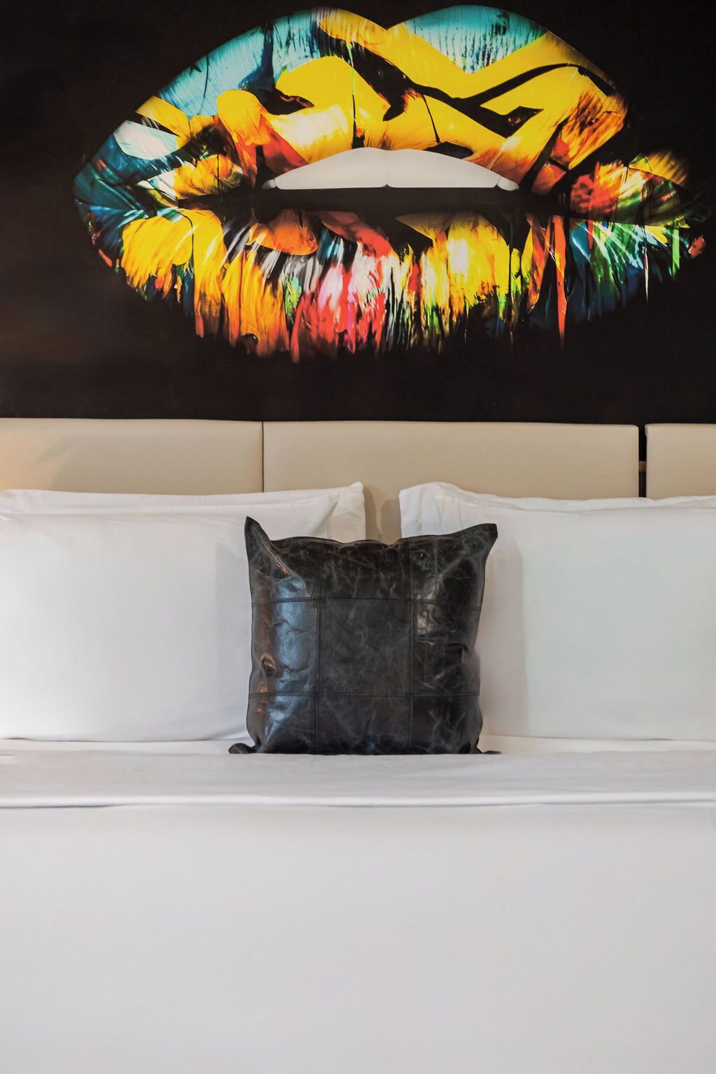 Un canapé blanc avec un coussin en cuir noir, dans une pièce où est accrochée une grande peinture abstraite au-dessus.