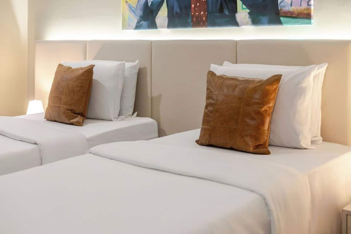 A hotel room with two beds, each with white bedding and brown pillows.