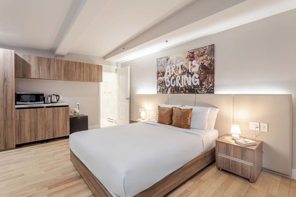 Un dormitorio moderno con una cama grande, armarios de madera, un microondas y un cuadro en la pared.
