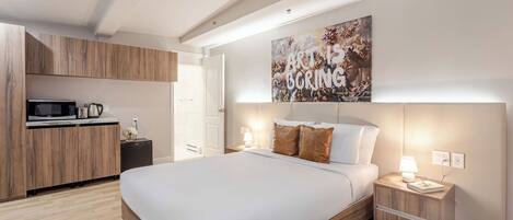 Un dormitorio moderno con una cama grande, armarios de madera, un microondas y un cuadro en la pared.