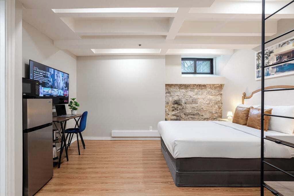 A modern bedroom with a bed, a desk with a computer, and a television.
