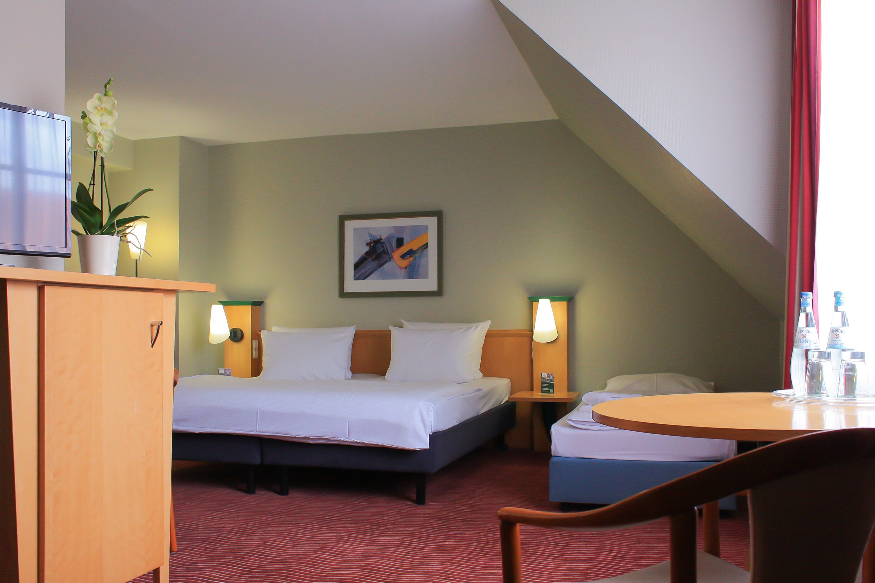 A hotel room with a bed, bedside tables, a desk, a chair, a television, and a potted plant.