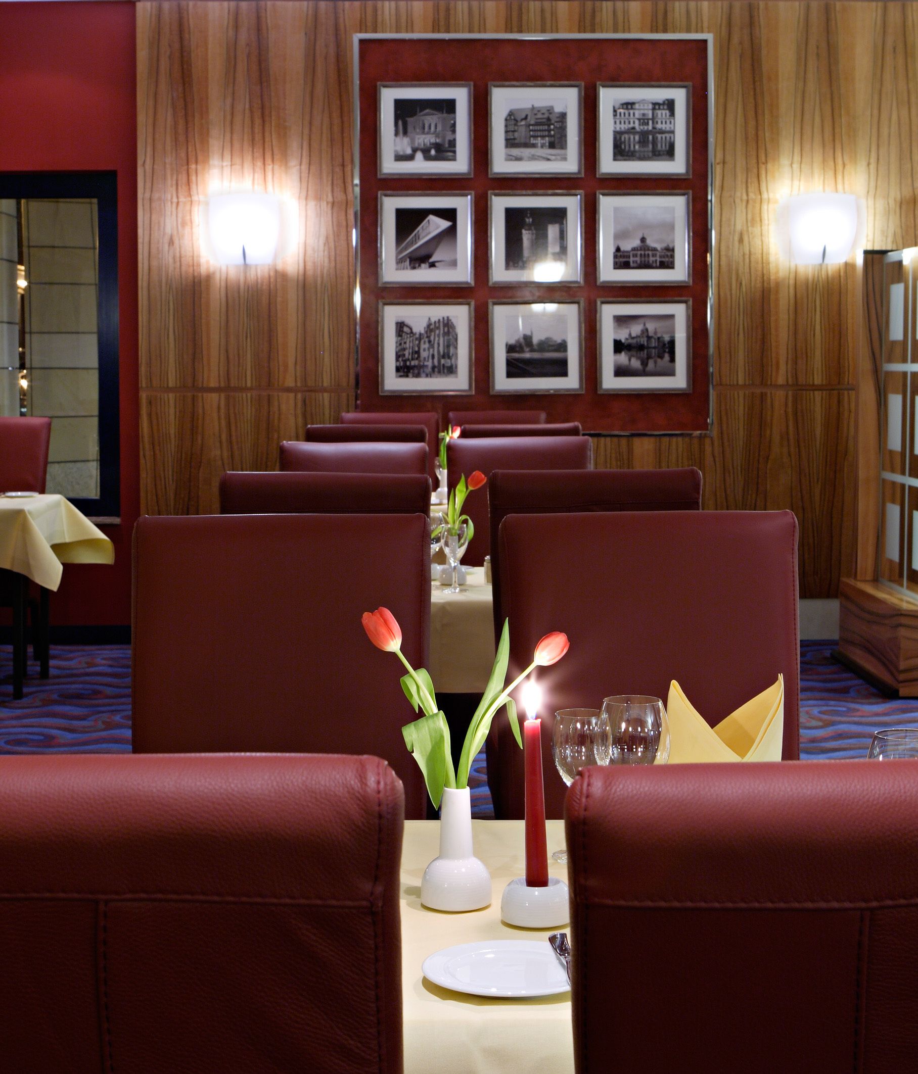 A restaurant with red leather chairs, a table with a vase of tulips, and framed pictures on the wall.