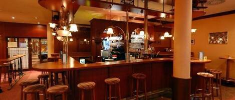 A bar area with multiple stools, a counter, and overhead shelves with bottles.