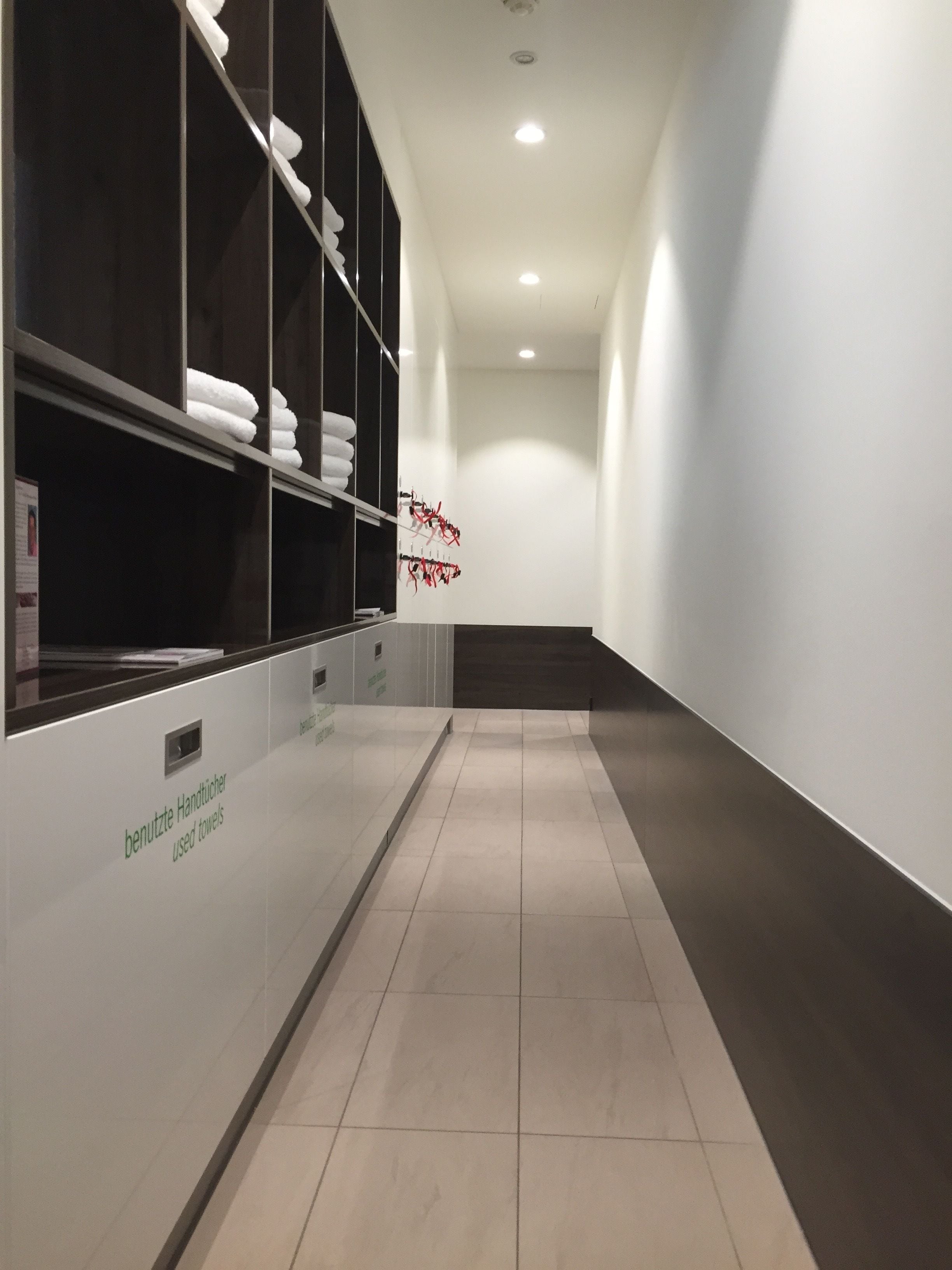 Un pasillo con pared blanca, piso de baldosas y repisa con toallas dobladas.