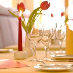 A table set for dining with clear glassware, a lit candle, and a vase with a single red tulip.