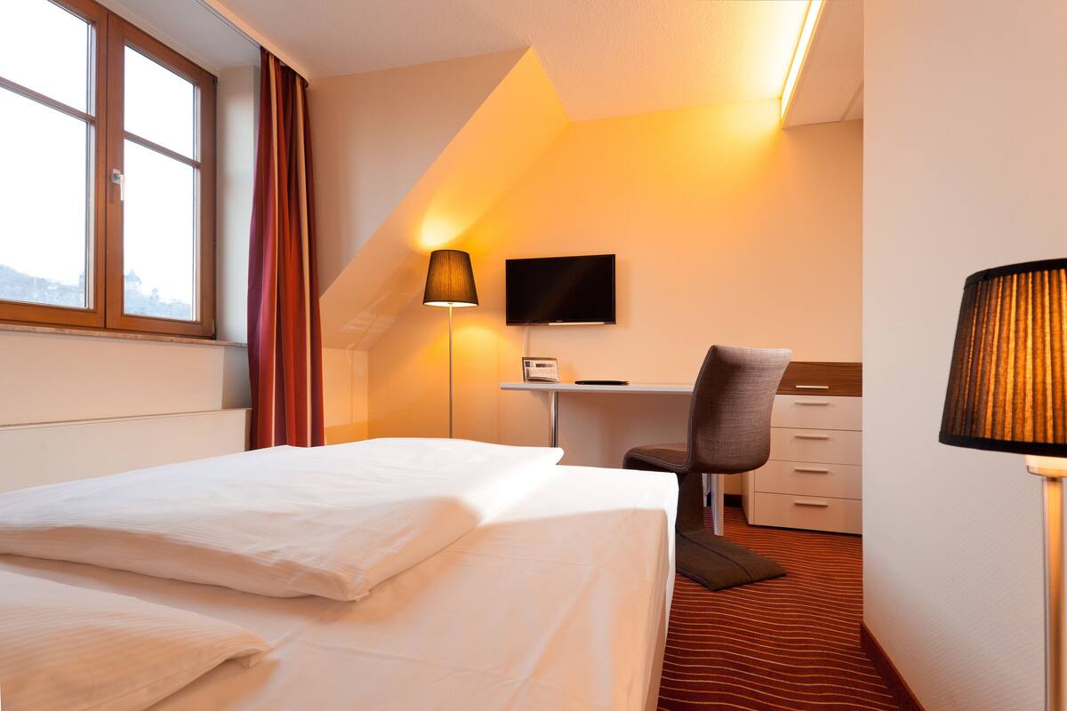 A hotel room with a bed, desk, chair, TV, and lamp.