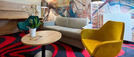 A modern living room with a sofa, a yellow armchair, a round table with a plant, and a colorful abstract wall mural.