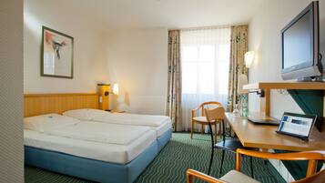 Een hotelkamer met twee bedden, een bureau met een laptop, een stoel, een televisie en een raam met gordijnen.