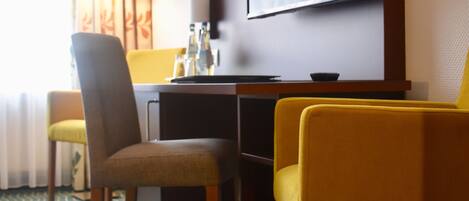 Habitación de hotel con escritorio, dos sillas, televisor y alfombra estampada.