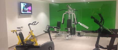 Un gimnasio con equipo de ejercicio, una televisión y paredes verdes.