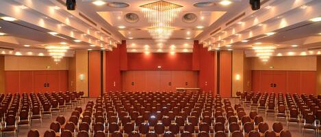 A large conference room with rows of chairs, a stage, and a chandelier.