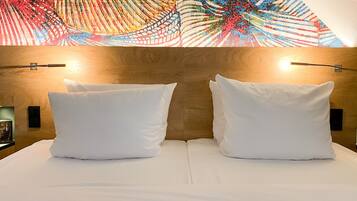 Habitación de hotel con cabecera de madera, dos almohadas blancas y una obra de arte abstracta y colorida sobre la cama.