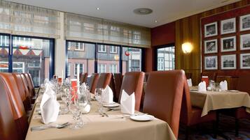 Un restaurant avec de longues tables dressées pour le repas, des fauteuils en cuir et des tableaux encadrés aux murs.