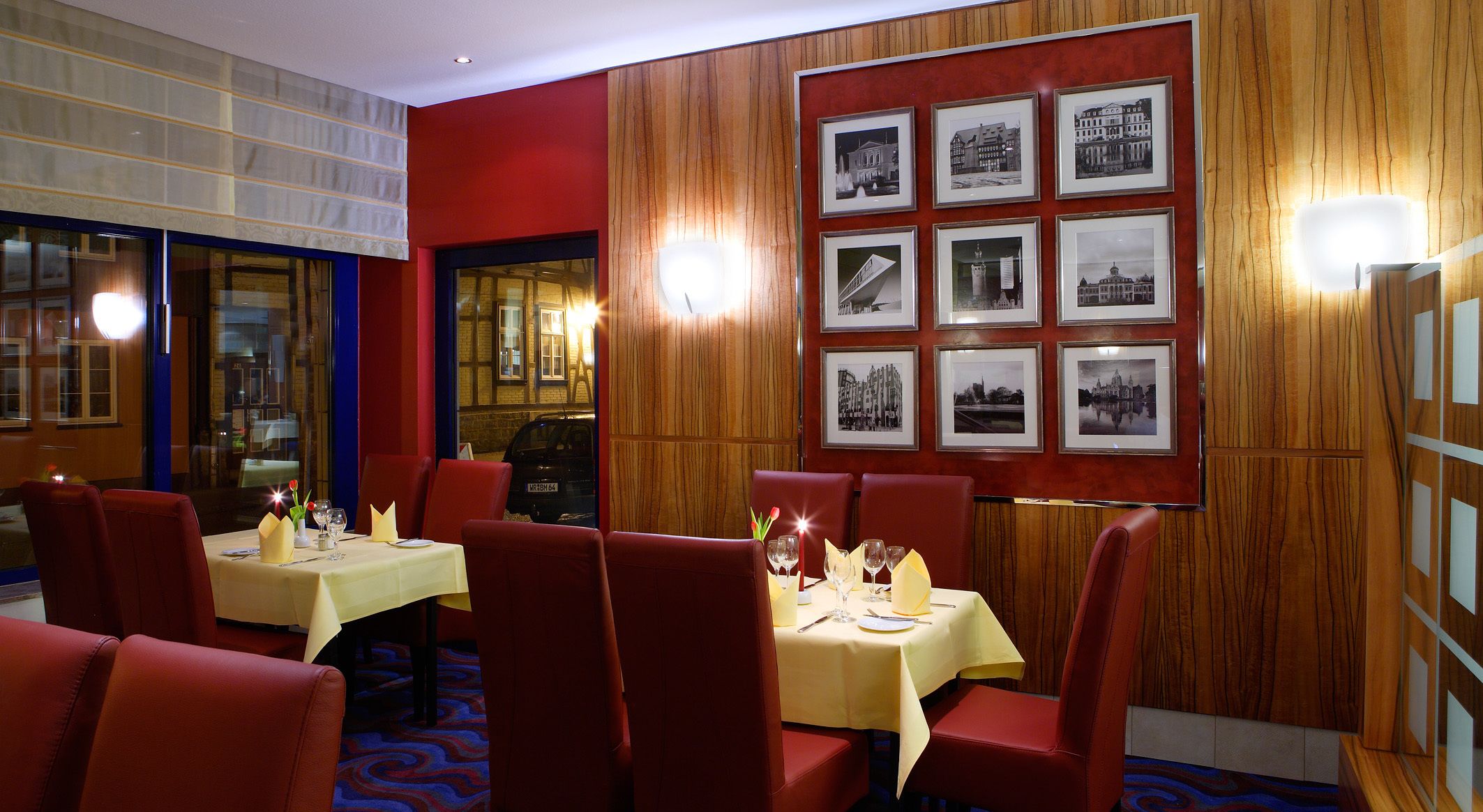 A restaurant with red upholstered chairs, yellow tablecloths, and framed black-and-white photographs on the wall.