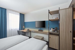 A hotel room with two beds, a desk with a flat-screen TV, a coffee maker, and a minibar. - H4 Hotel Leipzig (Leipzig)
